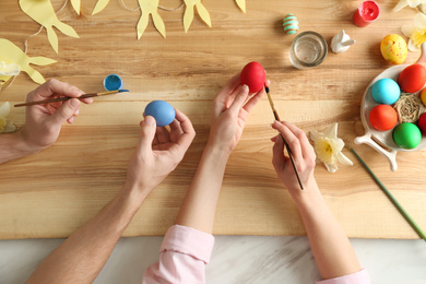 Photo of Couple painting Easter eggs at wooden table, top view