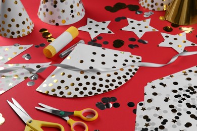 Photo of Handmade party hat templates, confetti and tools on red background