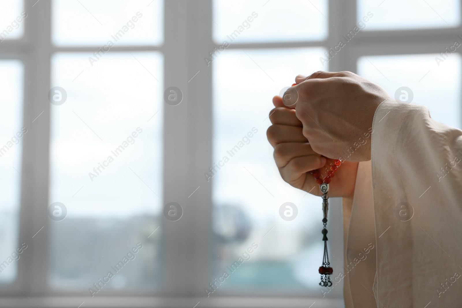 Photo of Muslim man with misbaha praying indoors, closeup. Space for text