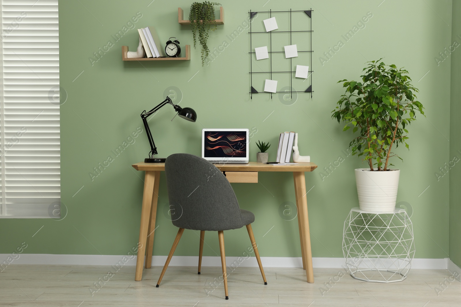 Photo of Workplace with modern laptop on wooden desk, potted plants and cosy chair at home