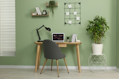Photo of Workplace with modern laptop on wooden desk, potted plants and cosy chair at home