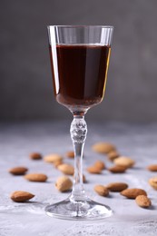 Photo of Liqueur glass with tasty amaretto and almonds on light grey table, closeup