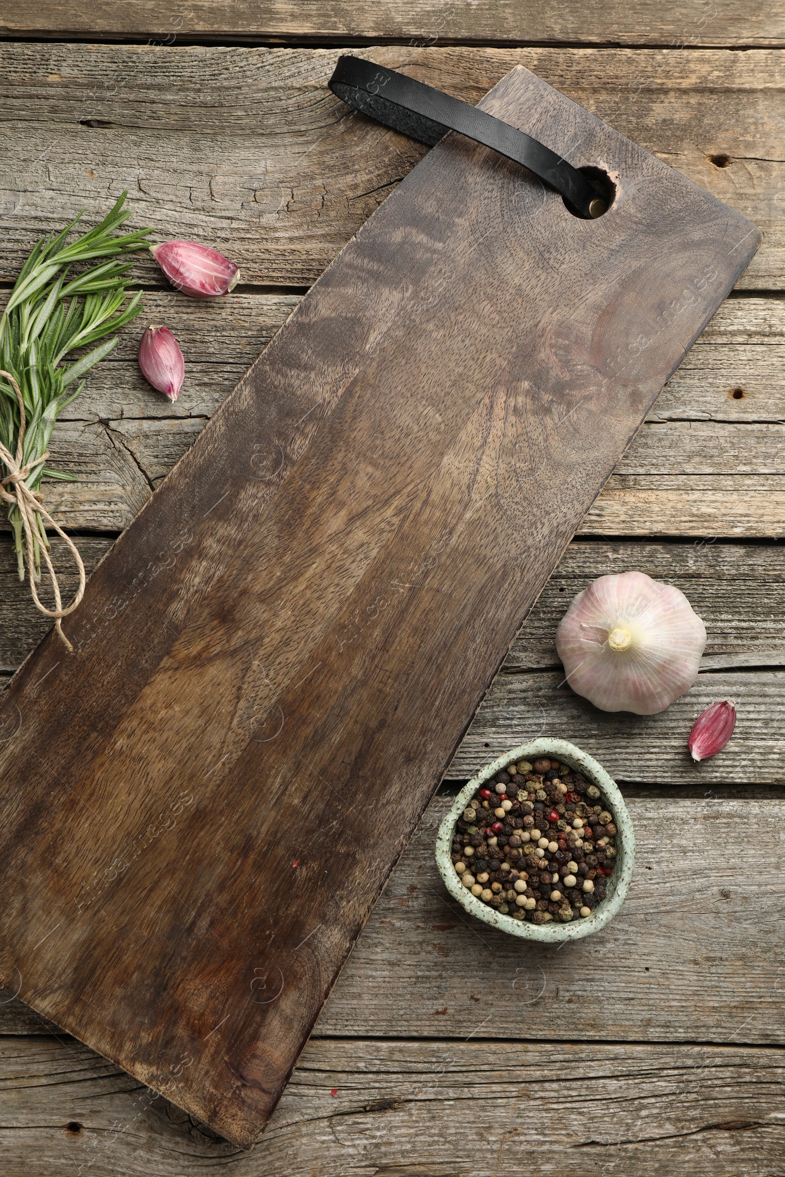 Photo of Cutting board, garlic, pepper and rosemary on wooden table, flat lay. Space for text