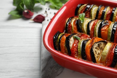Photo of Delicious ratatouille in baking dish on white wooden table, closeup. Space for text