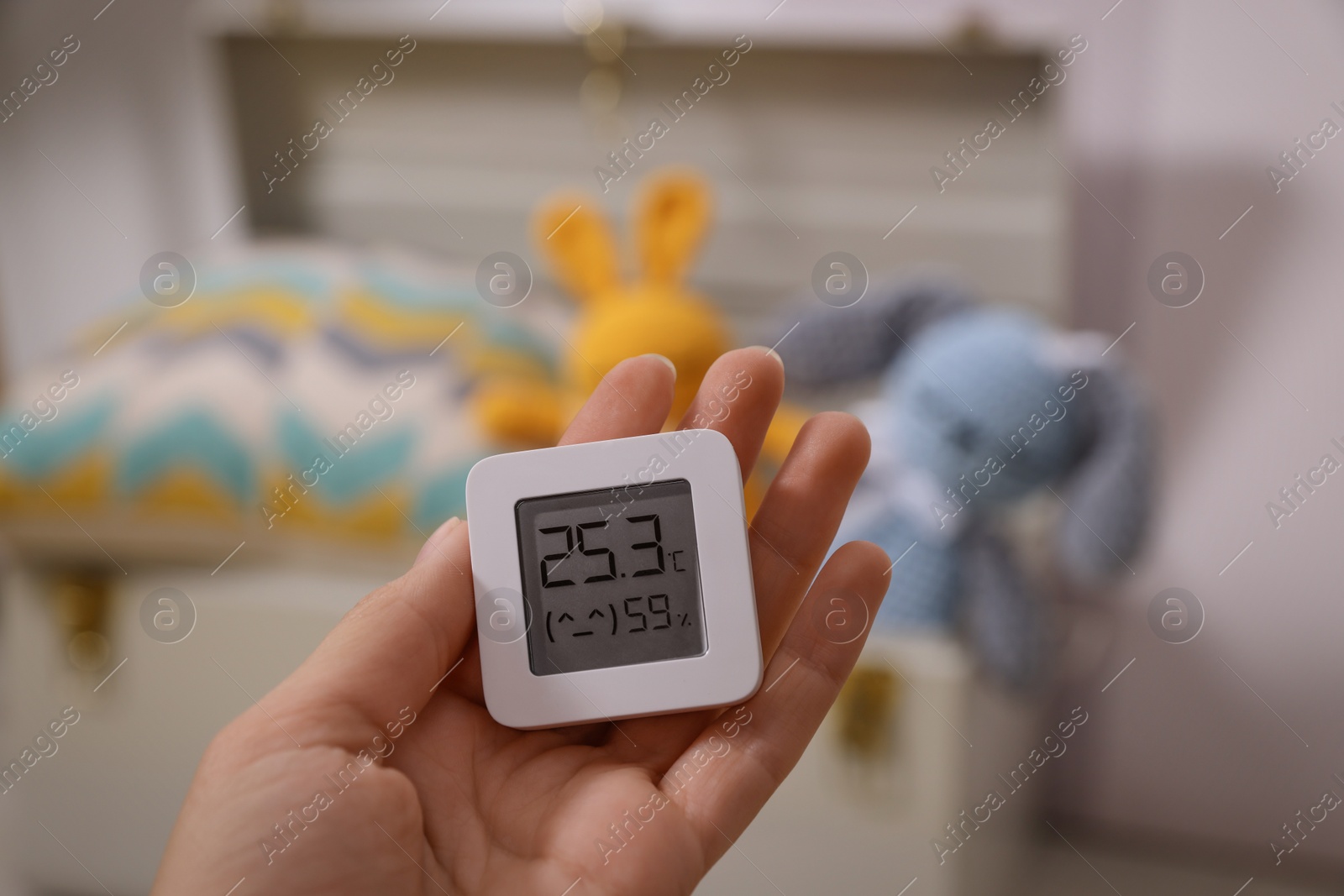 Photo of Woman holding digital hygrometer with thermometer on blurred background, closeup