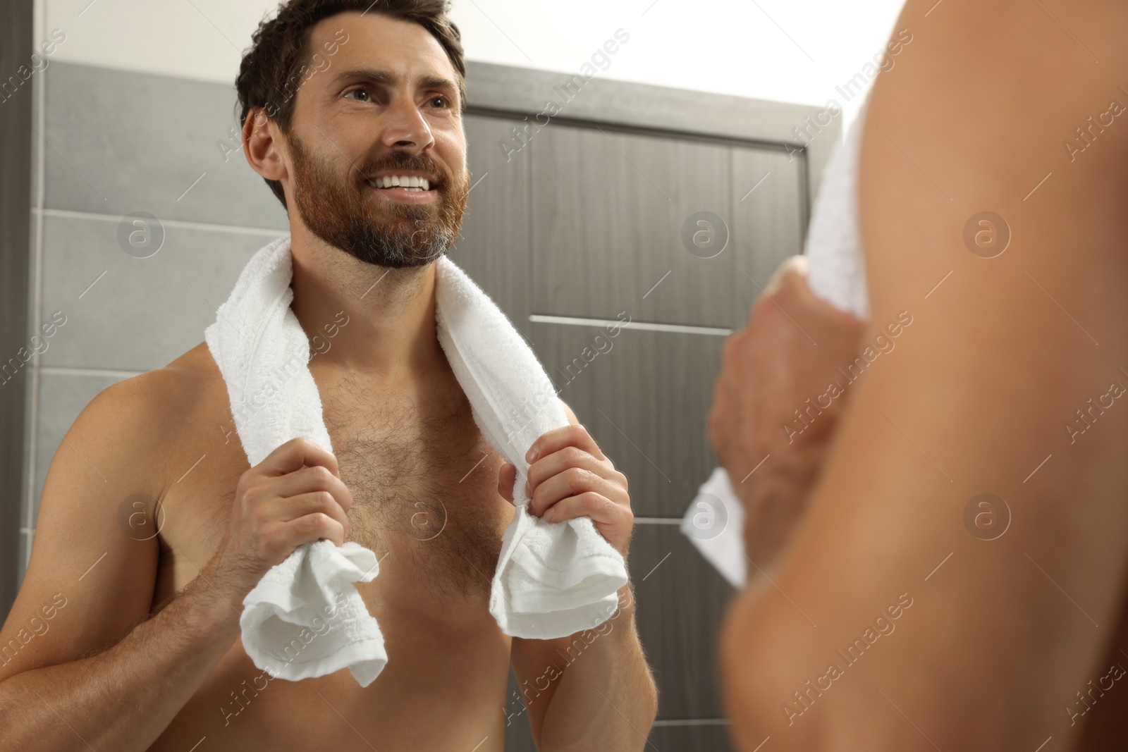 Photo of Handsome bearded man looking at mirror in bathroom near wooden doors