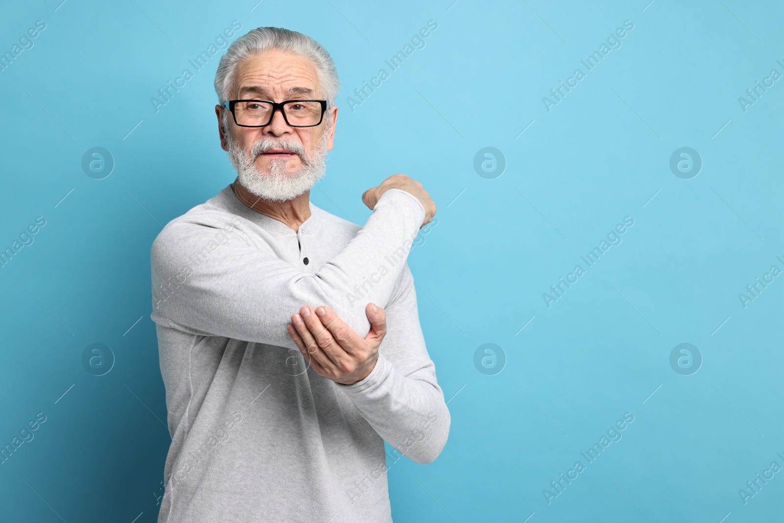 Photo of Arthritis symptoms. Man suffering from pain in elbow on light blue background, space for text