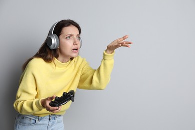 Confused woman in headphones with game controller on light grey background. Space for text