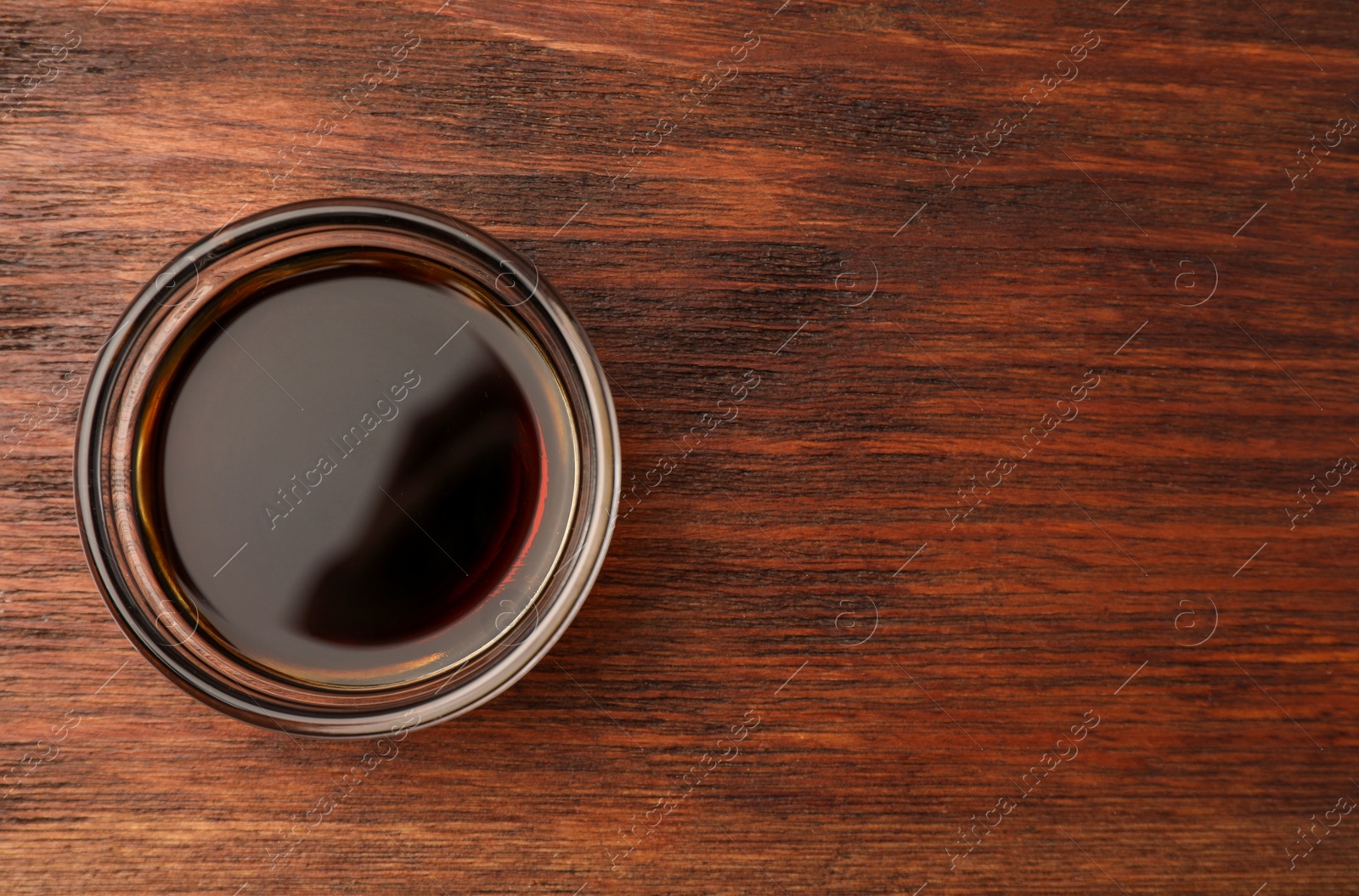 Photo of Bowl with soy sauce on wooden table, top view. Space for text