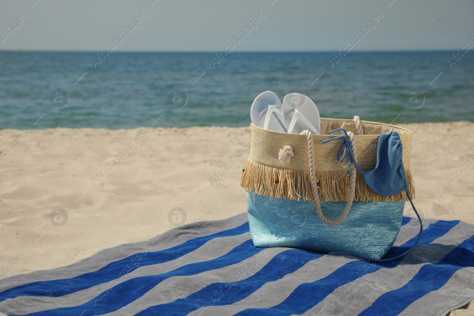 Photo of Beach towel with bag, flip flops and swimsuit on sand