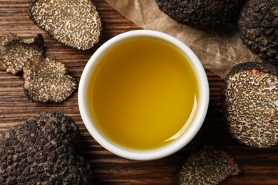 Photo of Fresh truffles and oil in bowl on wooden table, flat lay