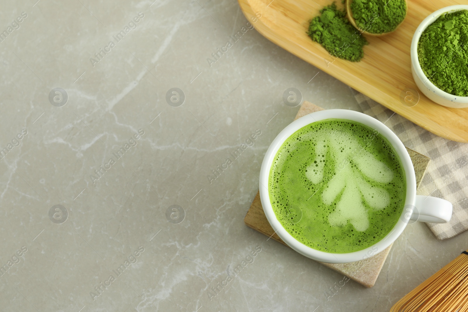 Photo of Cup of fresh matcha latte and green powder on light grey marble table, flat lay. Space for text