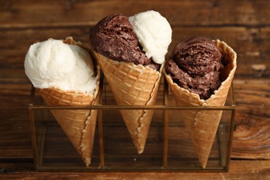 Tasty ice cream scoops in waffle cones on wooden table, closeup