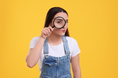 Photo of Confused young woman looking through magnifier glass on yellow background