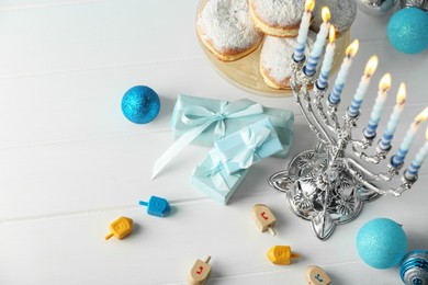 Composition with Hanukkah menorah, dreidels and gift boxes on white wooden table, above view. Space for text