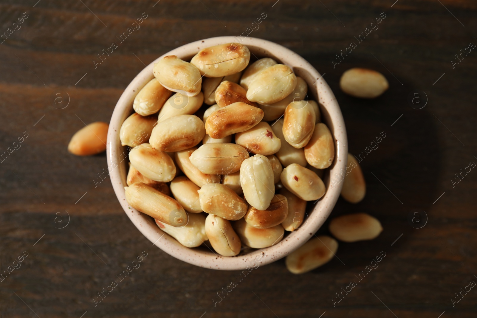 Photo of Roasted peanuts in bowl on wooden table, top view