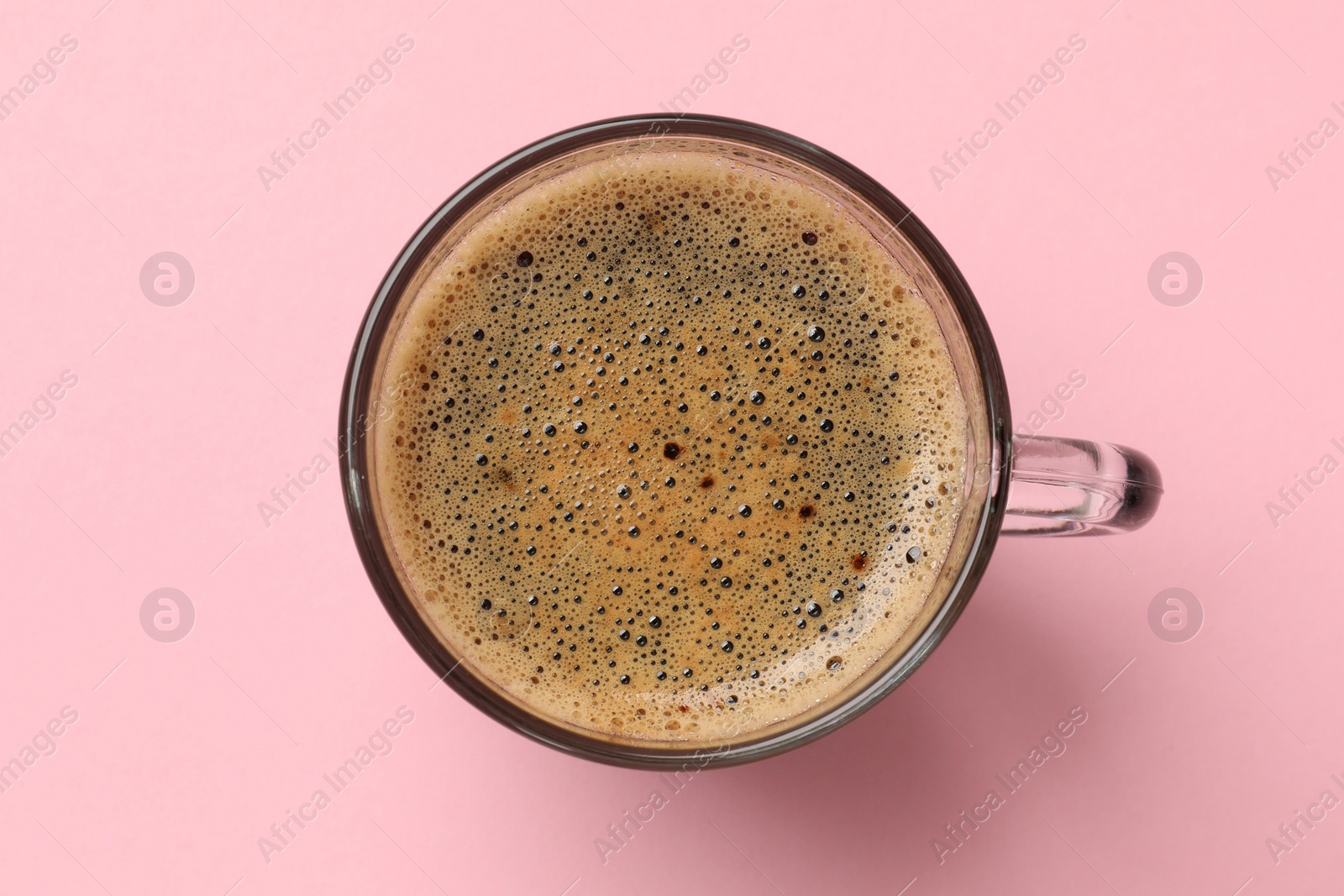 Photo of Aromatic coffee in glass cup on pink background, top view