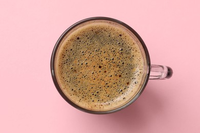 Aromatic coffee in glass cup on pink background, top view