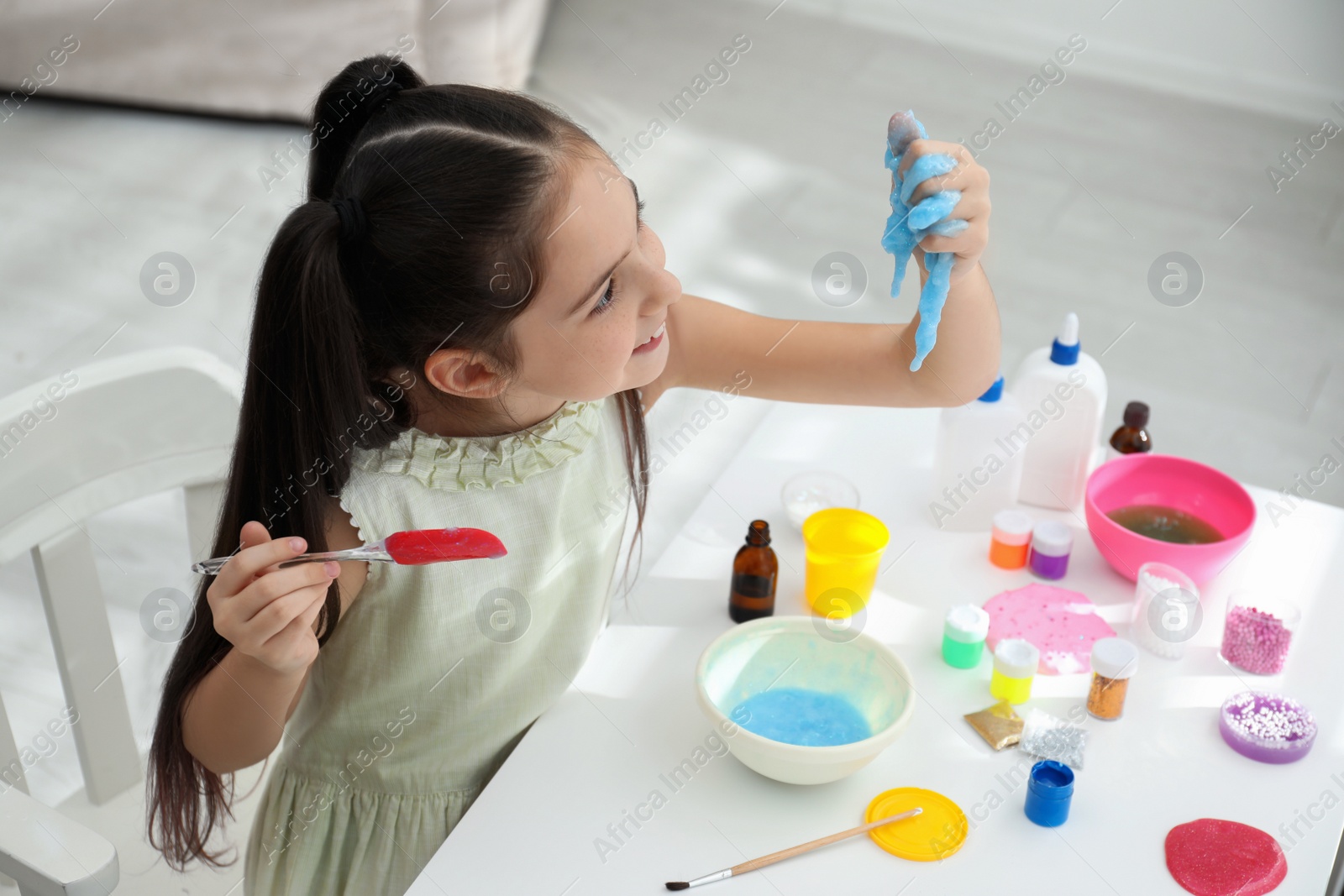 Photo of Cute little girl making DIY slime toy at table in room