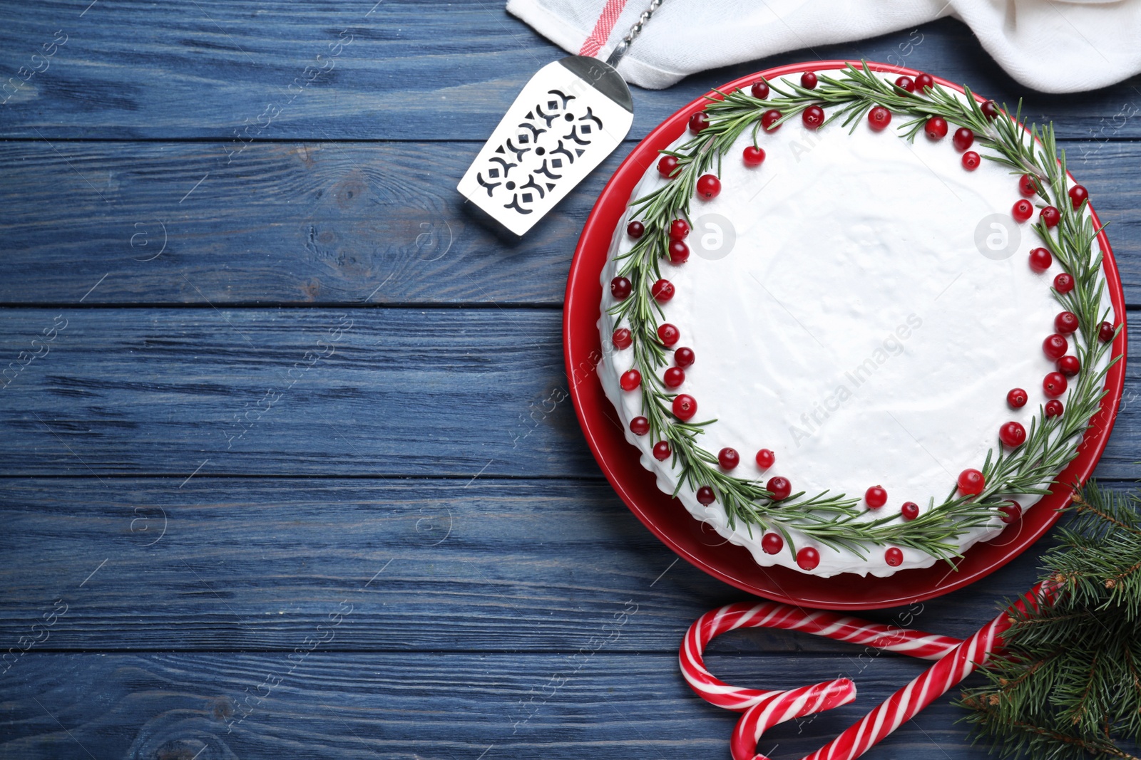 Photo of Traditional Christmas cake decorated with rosemary and cranberries on blue wooden table, flat lay. Space for text