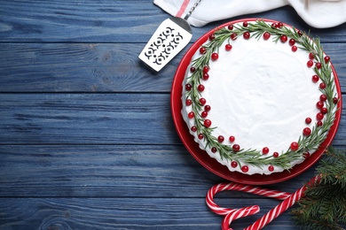 Traditional Christmas cake decorated with rosemary and cranberries on blue wooden table, flat lay. Space for text