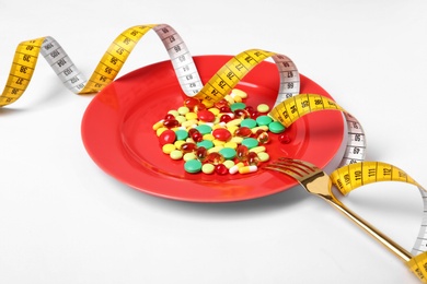 Plate with weight loss pills, fork and measuring tape on white background