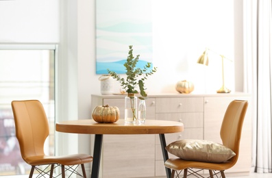 Photo of Beautiful living room interior with eucalyptus branches and decorative pumpkin on table