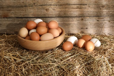 Photo of Fresh chicken eggs on dried straw bale near wooden wall