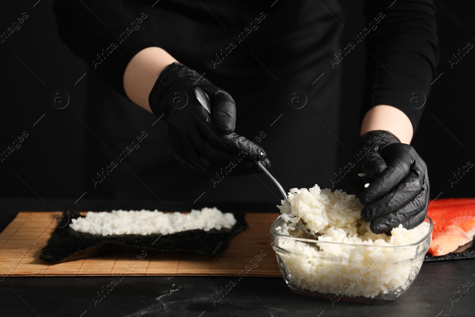 Photo of Chef in gloves making sushi roll at dark table, closeup