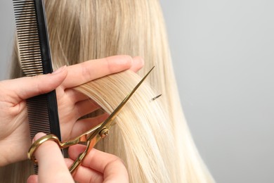 Hairdresser cutting client's hair with scissors on light grey background, closeup. Space for text