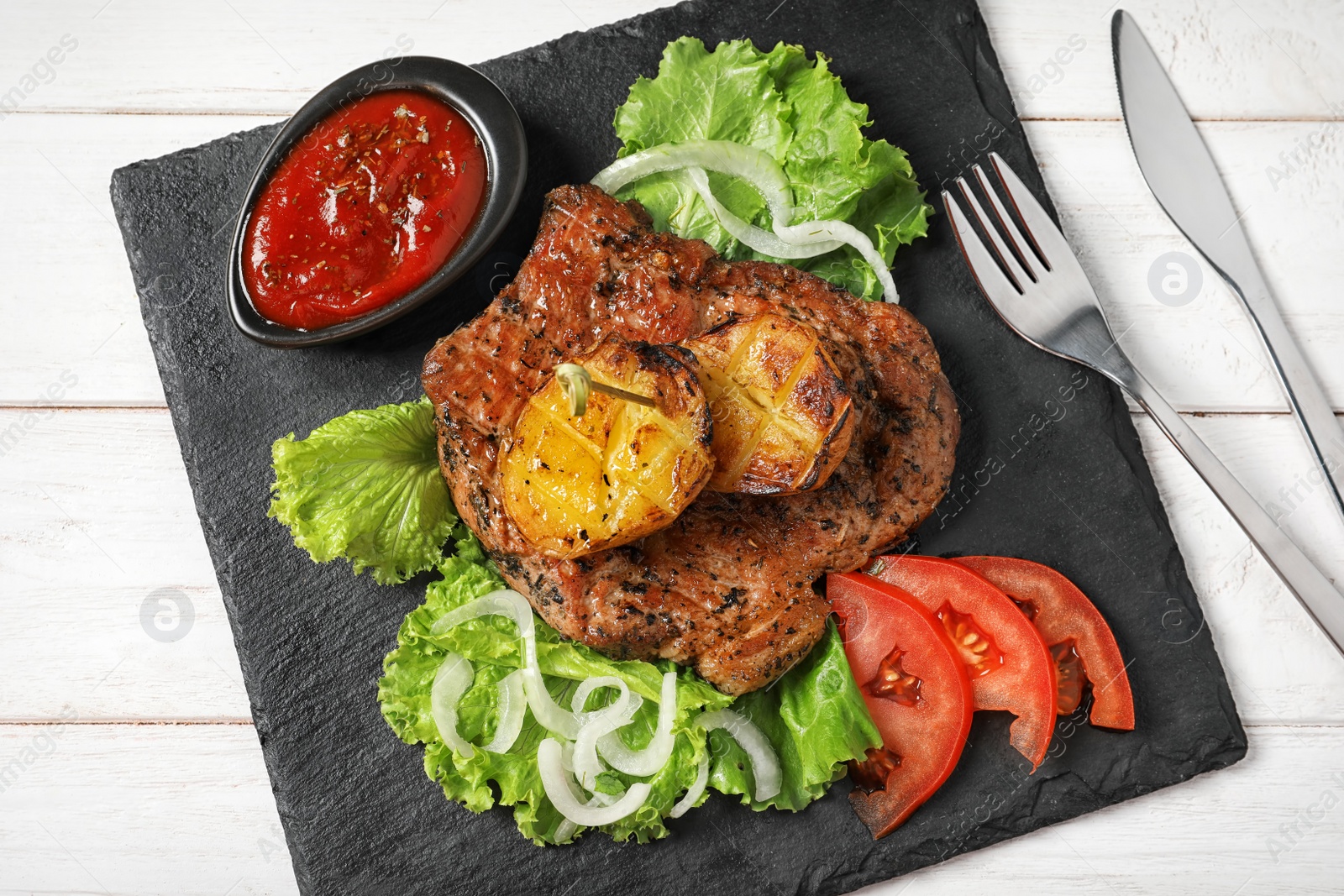 Photo of Slate plate with tasty grilled meat, potatoes and sauce on table, top view