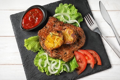 Photo of Slate plate with tasty grilled meat, potatoes and sauce on table, top view