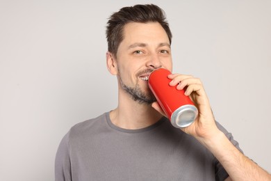 Happy man drinking from tin can on light grey background