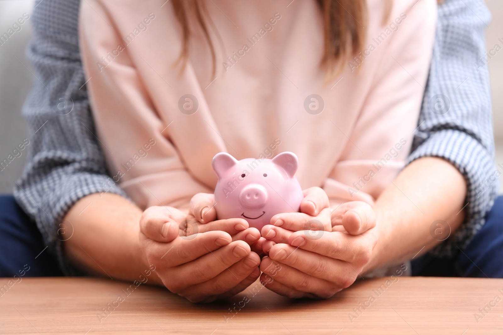 Photo of Couple with piggy bank at wooden table, closeup