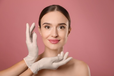 Photo of Doctor examining woman's face before plastic surgery on pink background