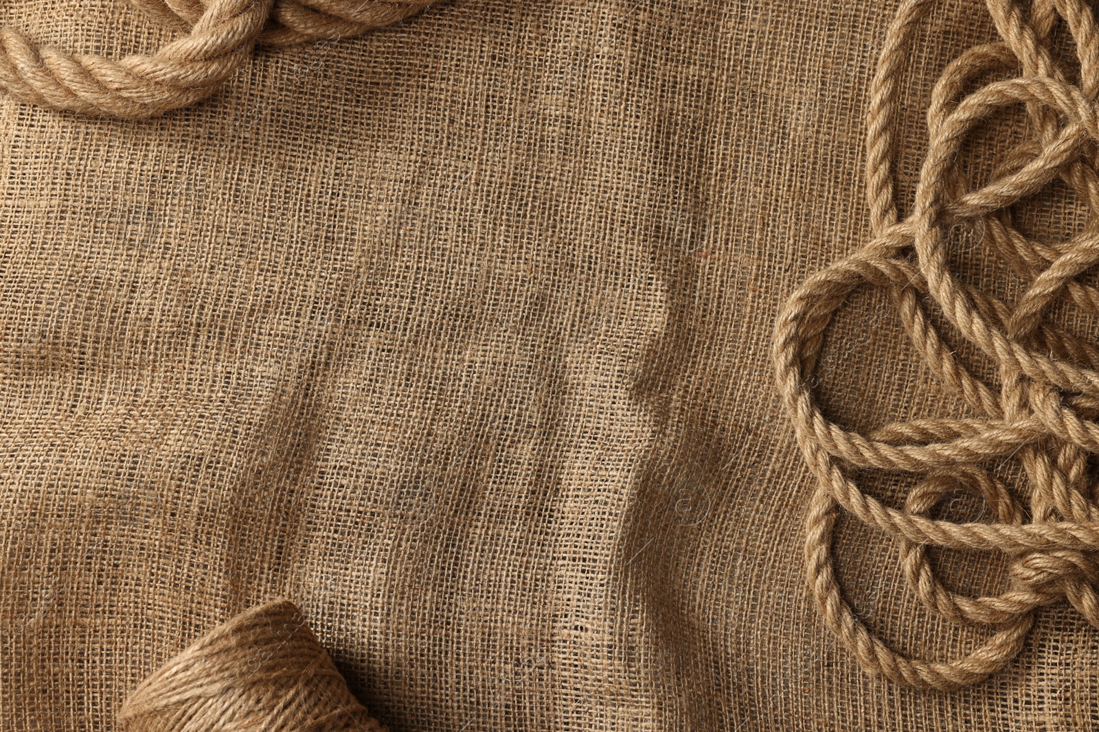 Photo of Spool of thread and natural brown jute on burlap fabric, top view