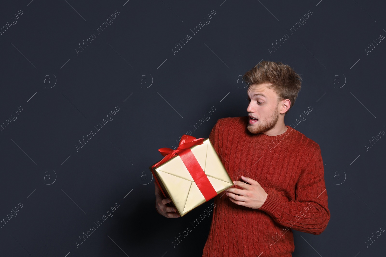 Photo of Emotional young man with Christmas gift on dark background. Space for text