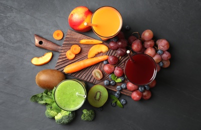 Photo of Delicious colorful juices in glasses and fresh ingredients on black table, flat lay
