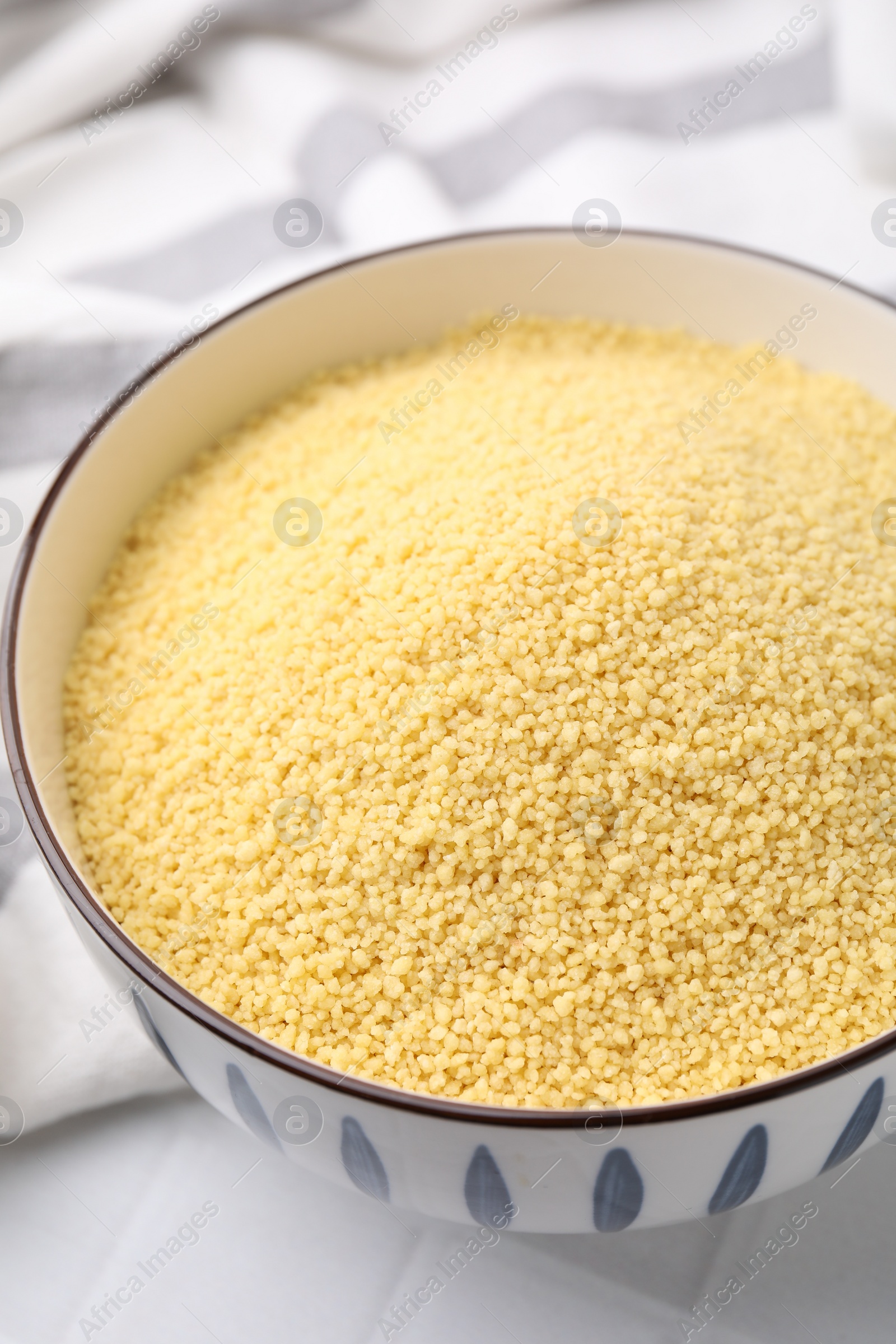 Photo of Raw couscous in bowl on table, closeup