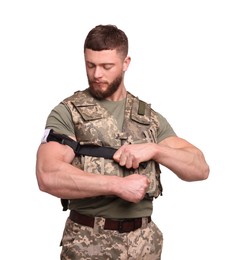 Soldier in military uniform applying medical tourniquet on arm against white background