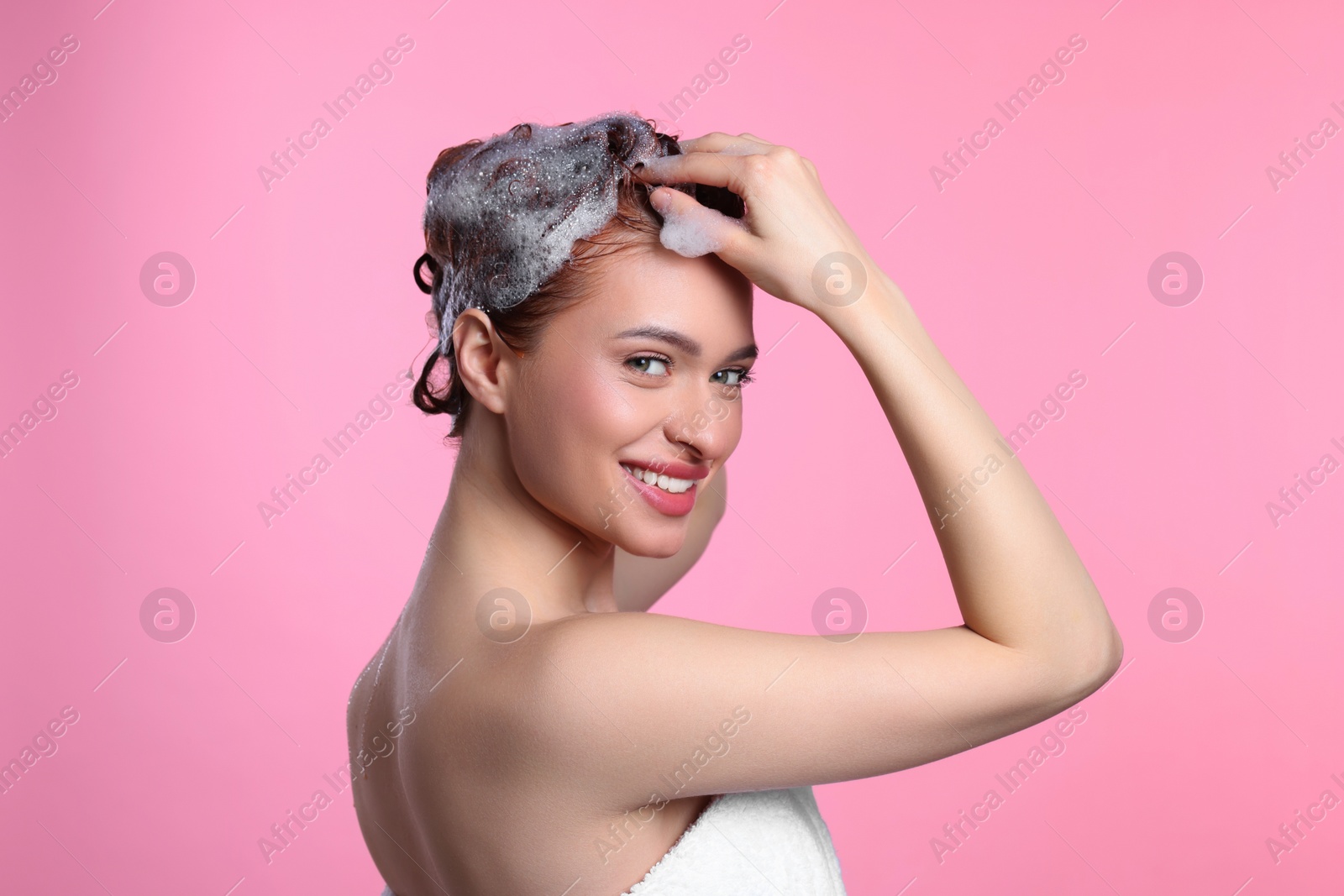 Photo of Happy young woman washing her hair with shampoo on pink background