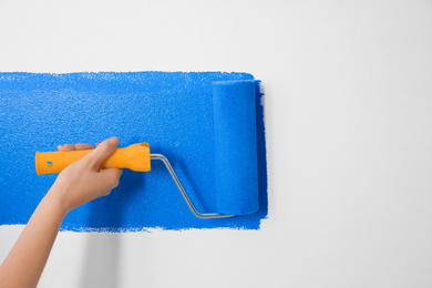 Woman painting white wall with blue dye, closeup. Interior renovation