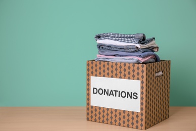 Photo of Donation box with clothes on wooden table against color background