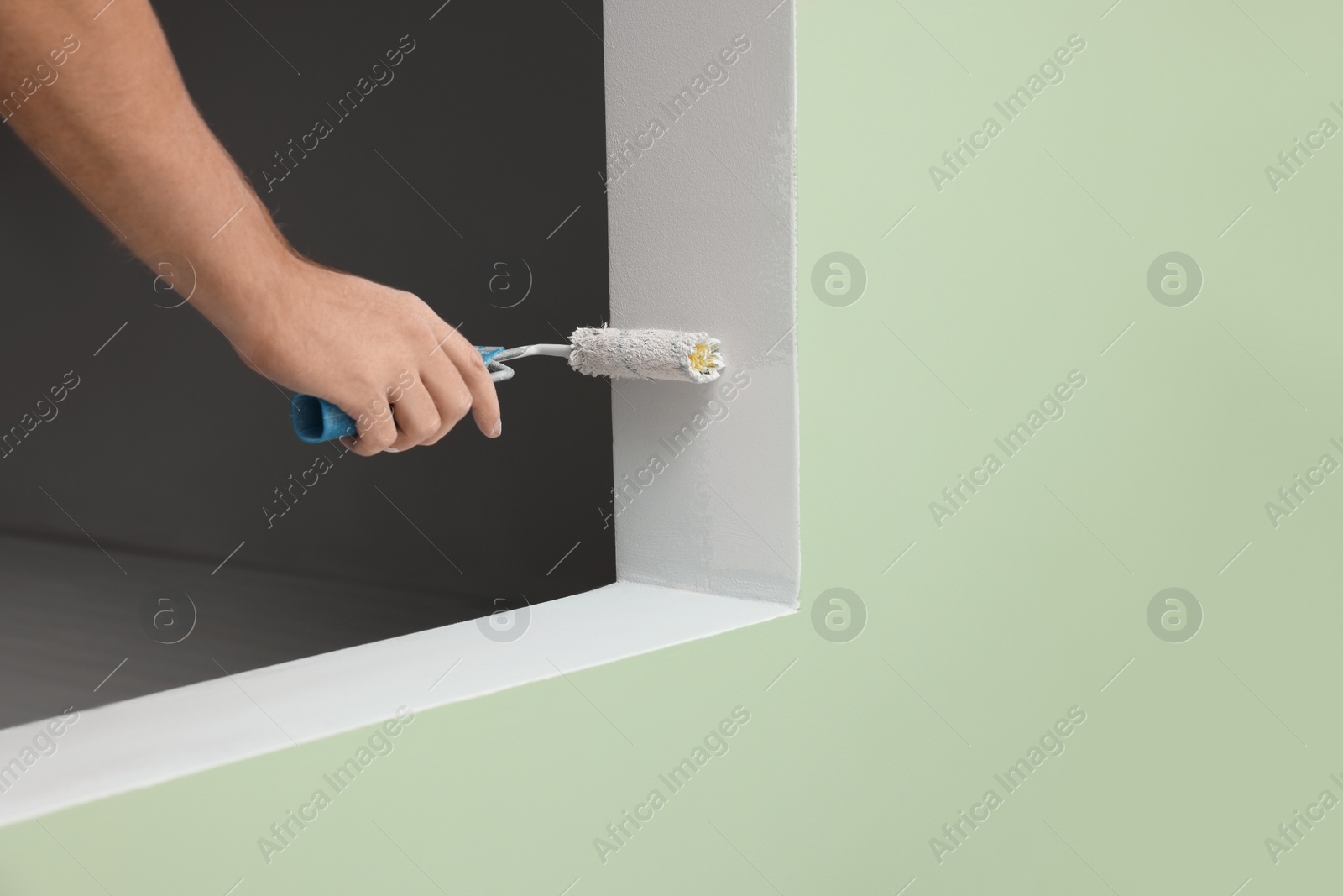Photo of Worker using roller to paint wall with white dye indoors, closeup