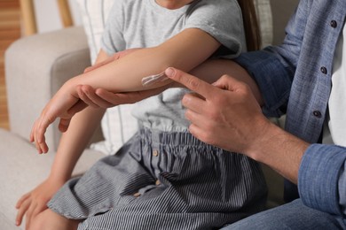 Photo of Father applying ointment onto his daughter's elbow on couch, closeup