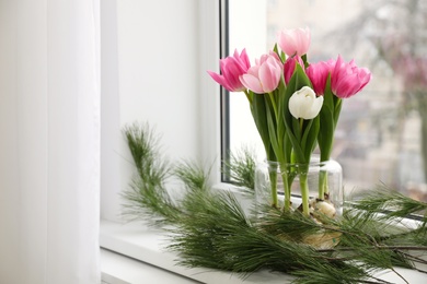 Photo of Beautiful tulips with bulbs and pine branches on window sill indoors. Space for text