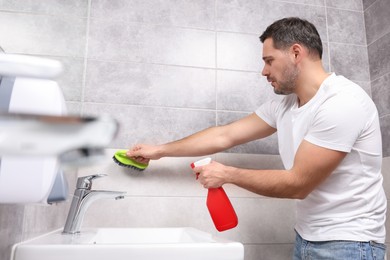 Photo of Man cleaning wall with sprayer and brush in bathroom