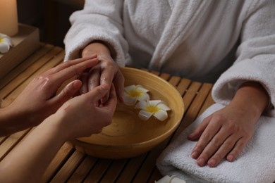 Photo of Woman receiving hand massage in spa salon, closeup. Bowl of water and flowers on wooden table