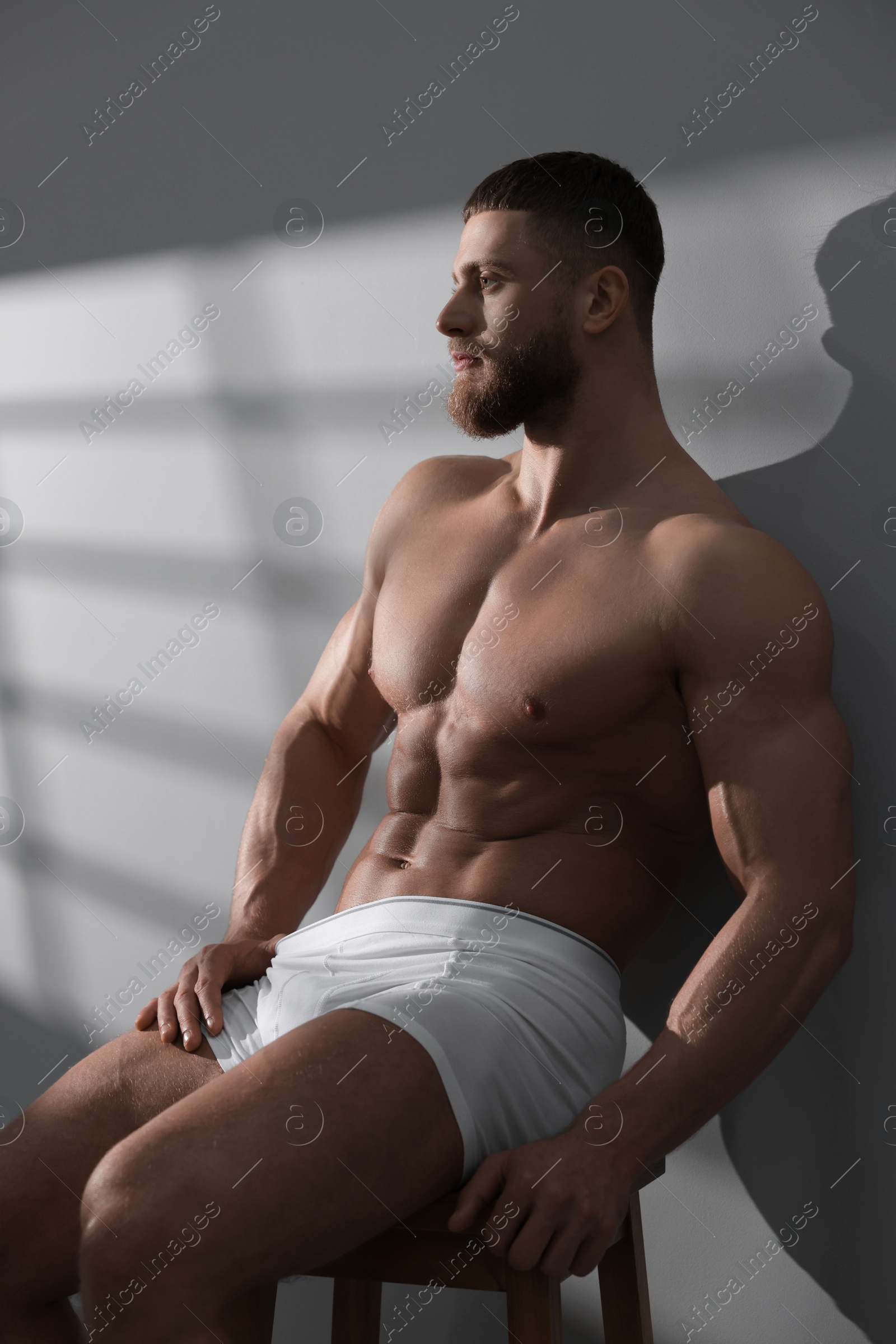 Photo of Young man in stylish white underwear sitting on chair near grey wall