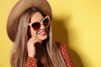 Young woman wearing stylish sunglasses and hat on yellow background